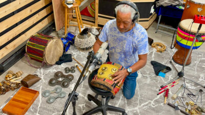 A photo of Bashiri Johnson playing percussion in the studio. 